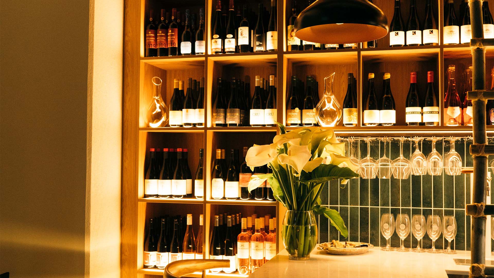 View behind the bar with wine bottles, branded glassware, and large vase of flowers