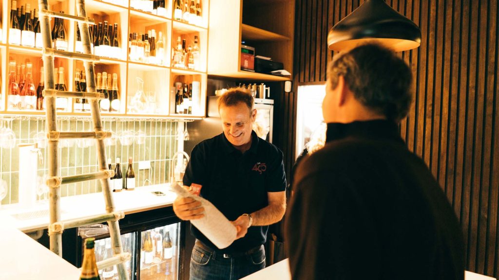 Michael Henley smiling behind the bar while regarding a bottle of wine.